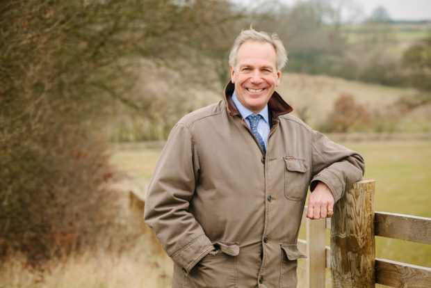 A man stands against a fence smiling into the camara