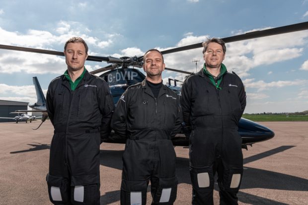 Three of the plant health team stand in a line facing the camara in front of a helicopter