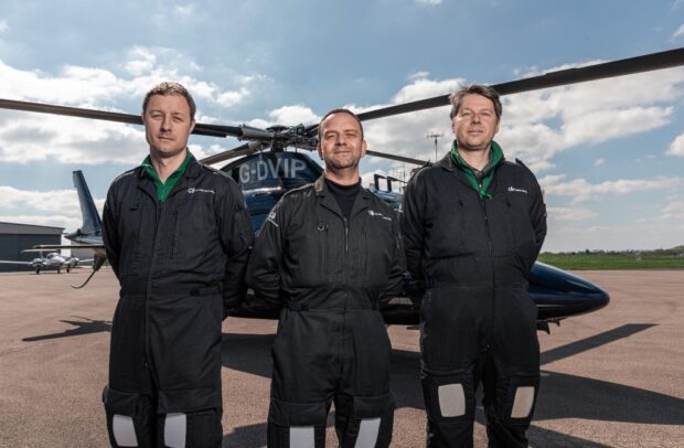 Three of the plant health team stand in a line facing the camara in front of a helicopter