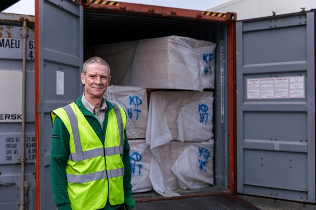 A man in a high vis jacket stands in front of a container full of wood products