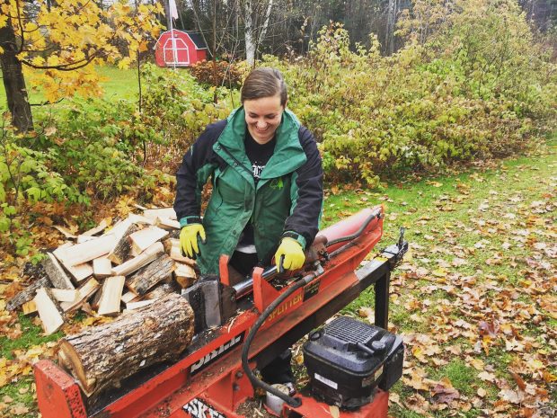 A woman smiling wearing a green coat using a log splitter