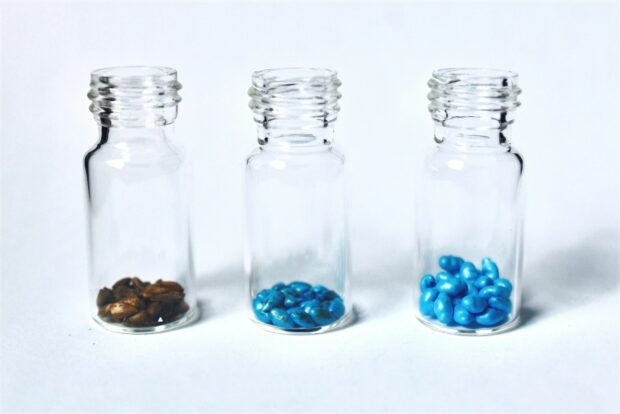 three glass bottles sit on a white background each filled a small amount with different coloured stones
