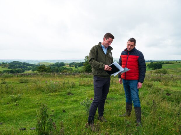 A PIES advisor stands with a landowner in a field showing him paperwork he has in his hand