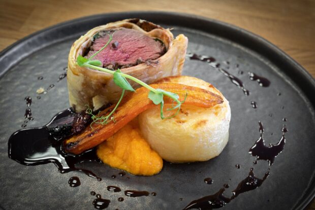 A plate of food showing a portion of vennison wrapped in pastry, pureed carrot a roasted carrot and some mashed potato